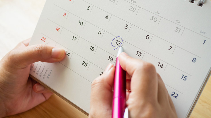 A person's hand circling a date on a calendar