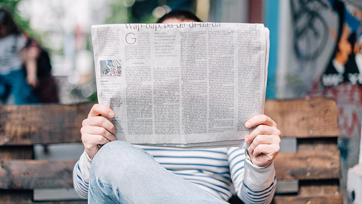 A person sitting on a bench and reading a newspaper