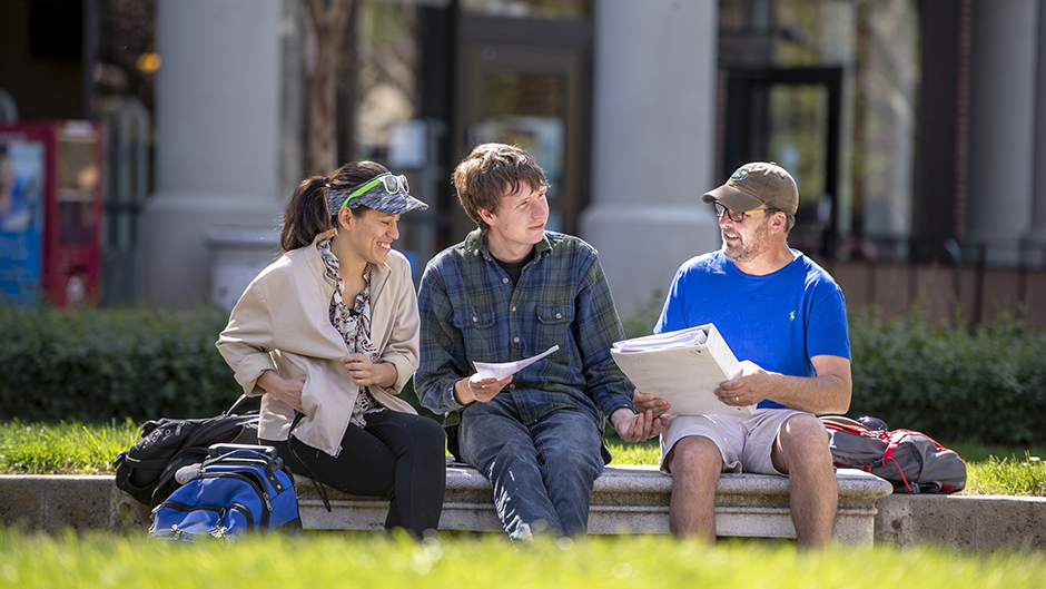 One female and two male SCC students sitting on stone bench talking and looking over their work.